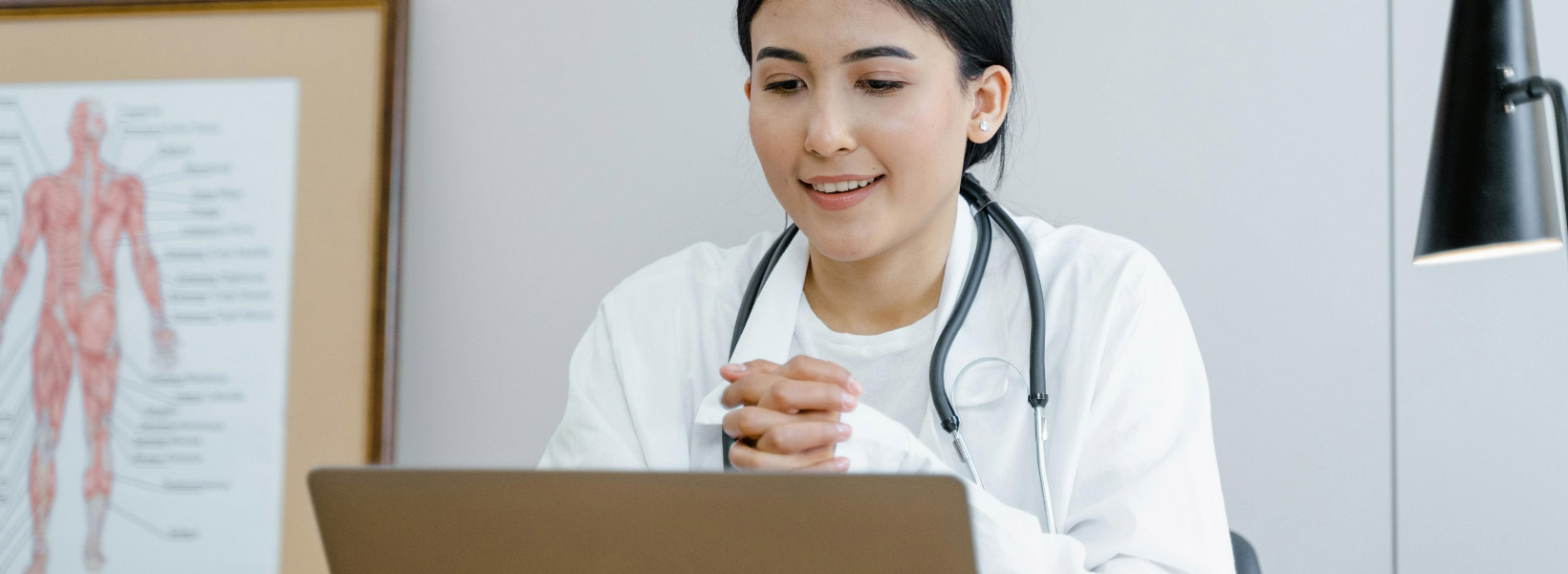 A female doctor wearing a mask, reviewing reports on a computer